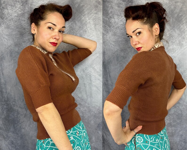 Pu&ograve; includere: Un maglione marrone a maniche corte con una trama a coste e una cerniera. Il maglione ha un colletto fantasia ed &egrave; abbinato a una gonna turchese con un disegno bianco e verde acqua. La persona indossa il rossetto rosso.