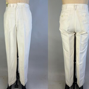 May include: Off-white trousers featuring a high-waisted design with a button and zip fly closure, belt loops, and a straight-leg cut. The back view displays two welt pockets with button closures, showcasing a clean, structured tailored appearance.