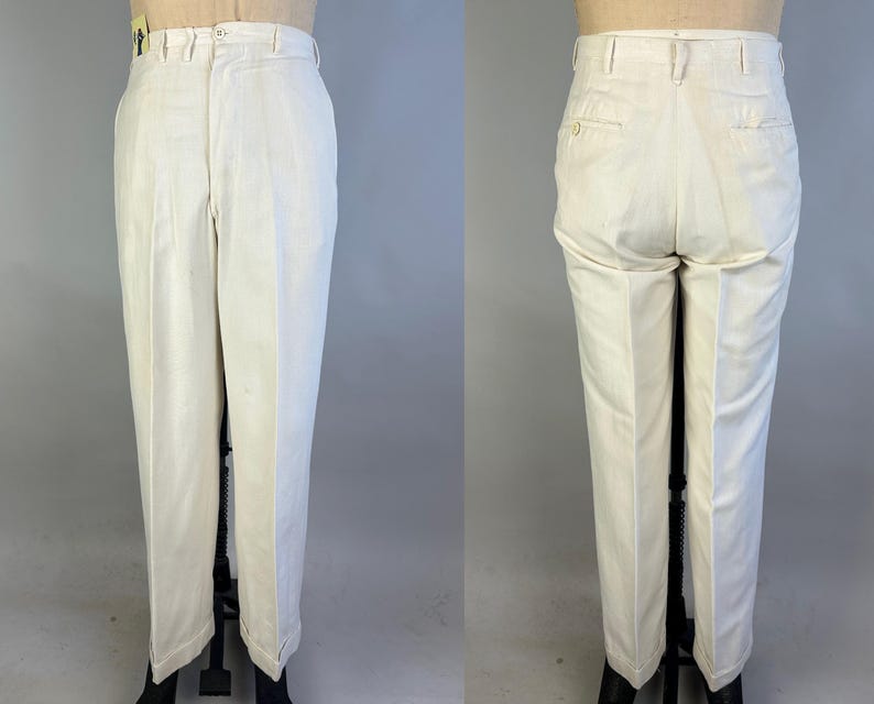 May include: Off-white trousers featuring a high-waisted design with a button and zip fly closure, belt loops, and a straight-leg cut. The back view displays two welt pockets with button closures, showcasing a clean, structured tailored appearance.