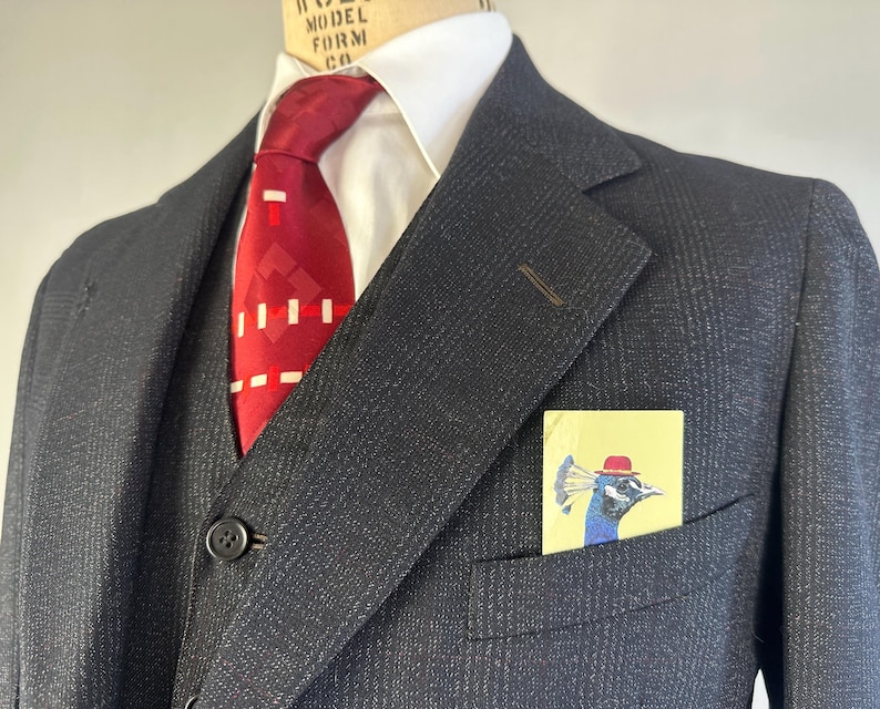 May include: A dark charcoal gray pinstriped suit jacket and vest worn over a crisp white collared shirt. A vibrant red necktie with a geometric white pattern is tied at the neck. A light yellow pocket square features a peacock wearing a red hat.