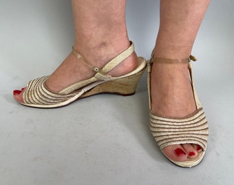 Puede incluir: Un par de sandalias de cuña beige con diseño a rayas y correas transparentes. Las sandalias tienen un dedo del pie abierto y un tacón de cuña tejido.