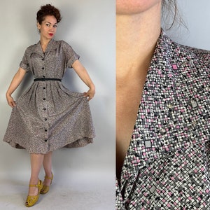 Może przedstawiać: Sukienka w stylu vintage zapinana na guziki z subtelnym wzorem w odcieniach szarości, różu i czerni. Posiada krótkie rękawy, kołnierzyk i czarny pasek. Sukienka sięga do kolan. Tkanina ma mały, powtarzalny geometryczny wzór.