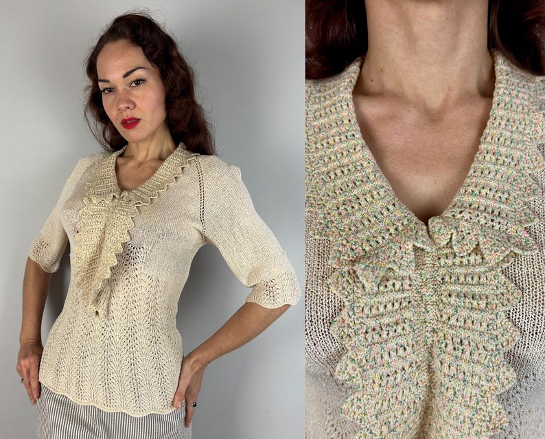 May include: A cream-colored crocheted sweater with a large, ruffled collar. The collar is made of a multi-colored yarn with shades of pink, green, and yellow.