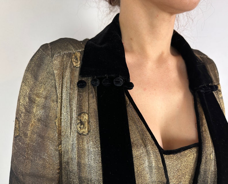 May include: A gold and black velvet robe with a deep V-neckline and a black velvet collar. The collar has a row of black pom-poms.