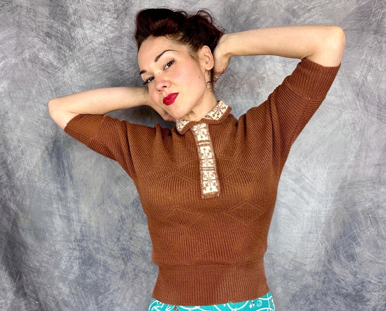 Pu&ograve; includere: Un maglione marrone a maniche corte con colletto decorativo. Il maglione ha una trama a coste e un motivo geometrico sul davanti. Il colletto presenta un design floreale color crema e beige.