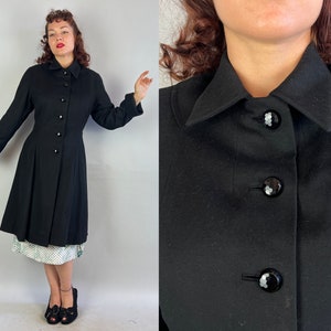 May include: A black wool coat with a large collar and a row of buttons down the front. The coat has a fitted bodice and a flared skirt.