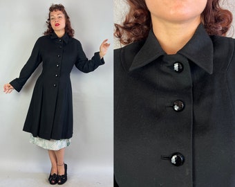 May include: A black wool coat with a large collar and a row of buttons down the front. The coat has a fitted bodice and a flared skirt.