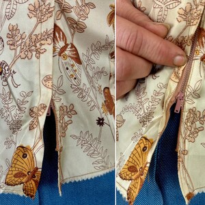 May include: Close-up of a cream-colored garment with a brown butterfly and floral pattern. The garment has a zipper closure and is made of a light fabric. The design includes detailed illustrations of butterflies and foliage.