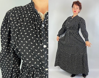 Puede incluir: Un vestido maxi negro con estampado floral blanco. El vestido tiene cuello alto, mangas largas y cintura fruncida. Está hecho de una tela ligera y tiene una silueta fluida.