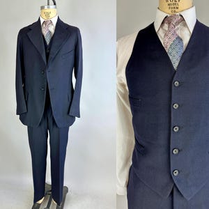 Puede incluir: Un traje azul marino con chaleco y corbata estampada. La chaqueta del traje tiene un cierre de un botón y el chaleco tiene cinco botones.