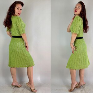 May include: A vintage lime green knit dress with short sleeves and a knee-length skirt. The dress features a black belt at the waist. The model is wearing gold-colored heels.