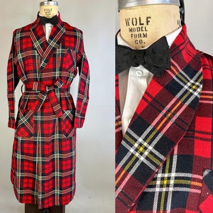 Op de afbeelding: Een rode, zwarte en gele geruite badjas met een zelfbindende riem. De badjas heeft een shawlkraag en twee klepzakken.