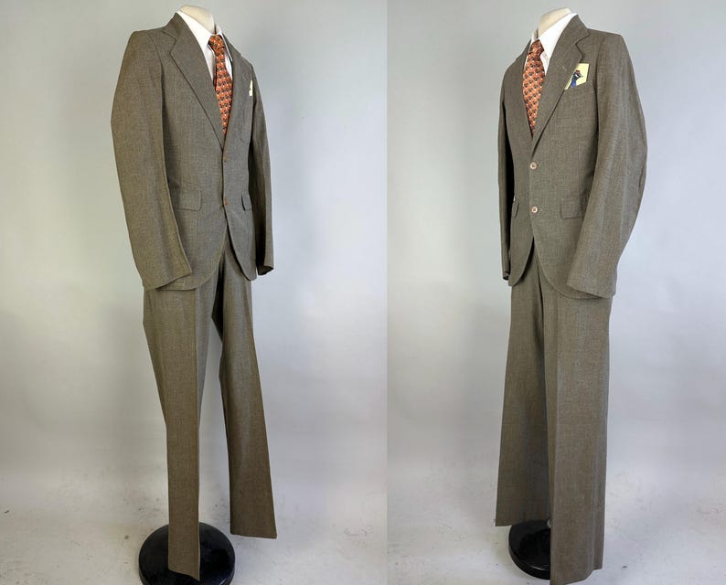 Op de afbeelding: Een tweedelig pak in een gedempte olijfbruine tint, bestaande uit een single-breasted colbert met twee knopen, inkepingen in de revers en klepzakken. Het pak bevat een bijpassende broek, een wit overhemd met kraag en een das met patroon.