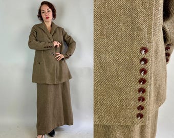 May include: A brown tweed skirt suit with a long skirt and a double-breasted jacket. The jacket has brown buttons and a pointed collar.