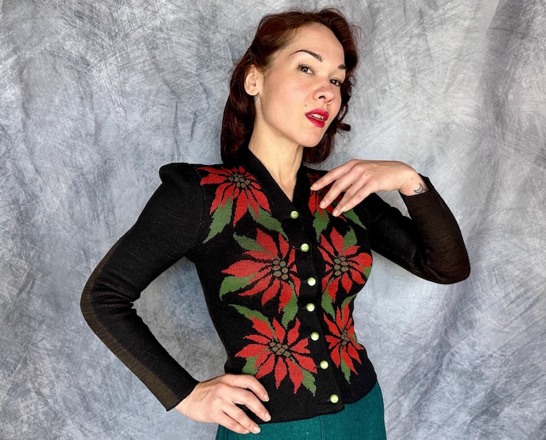 May include: Black knit cardigan with red and green floral design. The long-sleeved sweater features a V-neck and is buttoned up the front with gold-colored buttons. The floral pattern is a poinsettia design.