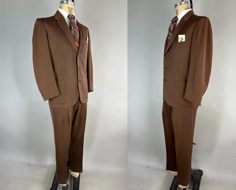 May include: A brown suit displayed on a mannequin. The suit includes a blazer with two front pockets, a matching pair of trousers, a white dress shirt, and a patterned tie. A small card is in the blazer's pocket.