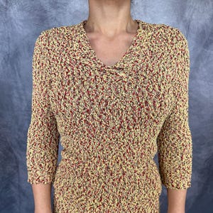 May include: A textured knit top with a V-neck and three-quarter sleeves. The top features a speckled pattern in yellow, red, and brown. The garment is made of a soft, comfortable material.