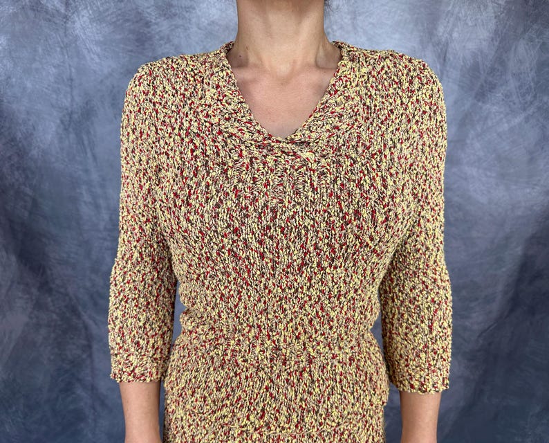 May include: A textured knit top with a V-neck and three-quarter sleeves. The top features a speckled pattern in yellow, red, and brown. The garment is made of a soft, comfortable material.