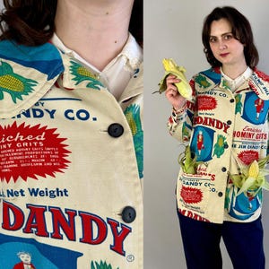 May include: Cream-colored jacket with a colorful print featuring corn and the text "DANDY CO." and "Enriched Hominy Grits." The jacket has a collared neckline, black buttons, and two pockets. The design includes red, blue, and green accents.