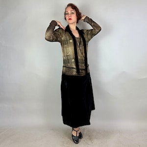 May include: A woman wearing a gold and black patterned dress with a long black velvet skirt. The dress has a V-neckline and long sleeves.