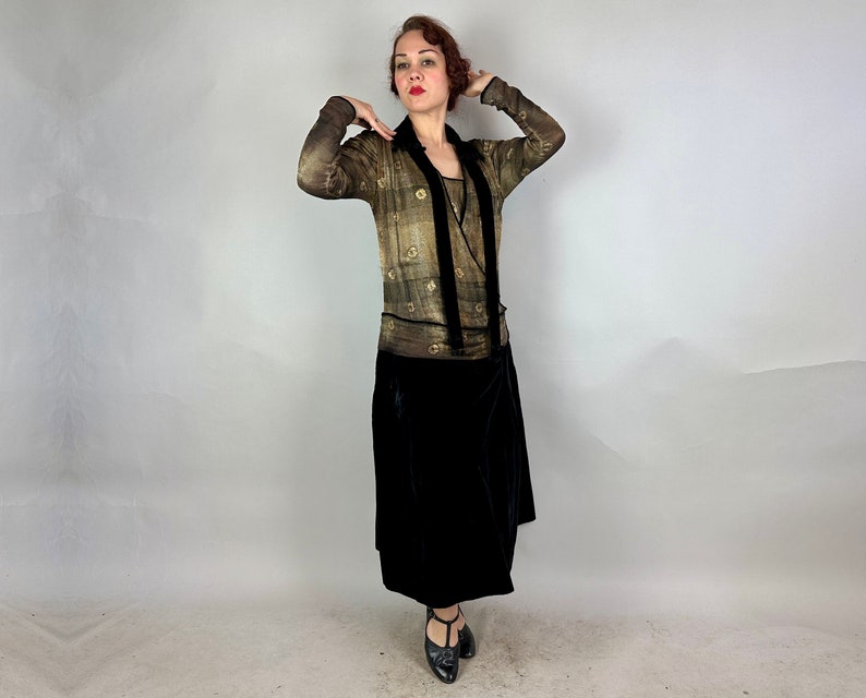 May include: A woman wearing a gold and black patterned dress with a long black velvet skirt. The dress has a V-neckline and long sleeves.