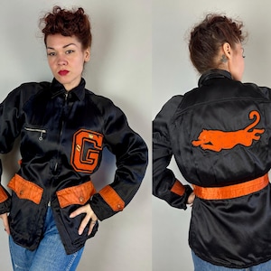 Op de afbeelding: Zwarte satijnen jas met oranje details, waaronder een grote "G" patch en een rennende tijger op de rug. De jas heeft een ritssluiting, oranje zakken en een bijpassende riem. Een kledingstuk in vintage stijl.