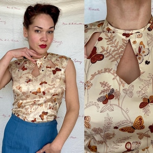 May include: A cream-colored sleeveless top with a keyhole neckline and a butterfly pattern in shades of brown and orange. The top is made of a silky material and has a vintage aesthetic.