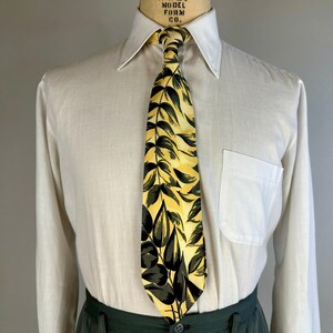 May include: A white dress shirt with a long sleeve and a yellow and green patterned tie. The tie has a leafy design.