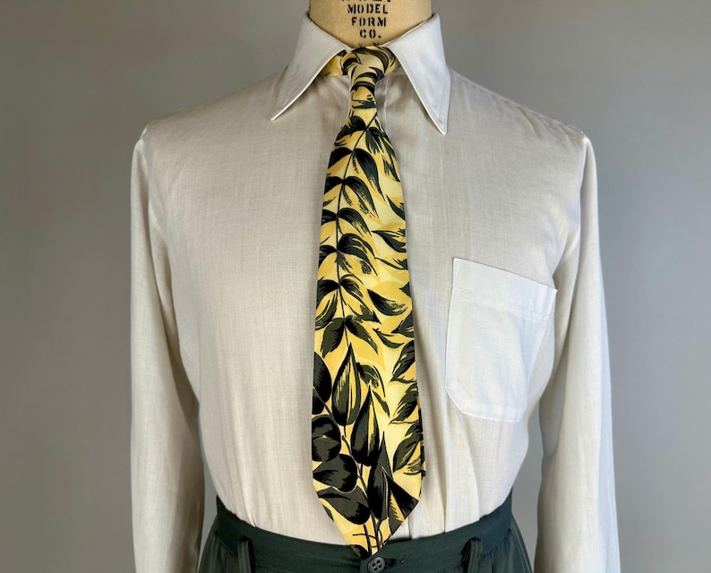 May include: A white dress shirt with a long sleeve and a yellow and green patterned tie. The tie has a leafy design.