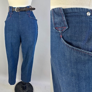 May include: High-waisted dark blue denim trousers featuring a front zipper closure, a silver-tone metal button, and distinctive red contrast stitching along the pockets and waistband. A thin dark brown textured leather belt is threaded through loops.