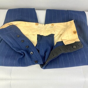 Puede incluir: Un pantal&oacute;n azul con rayas diplom&aacute;ticas blancas, con un dise&ntilde;o de cintura alta y forro interior de color crema. La prenda incluye un cierre de botones oscuros y botones adicionales a lo largo de la cinturilla interior.