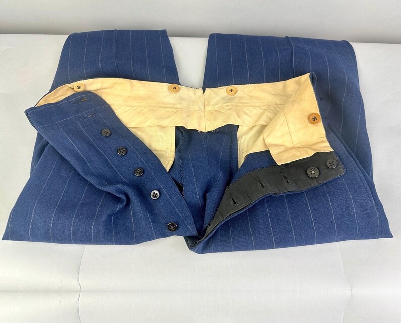 Puede incluir: Un pantal&oacute;n azul con rayas diplom&aacute;ticas blancas, con un dise&ntilde;o de cintura alta y forro interior de color crema. La prenda incluye un cierre de botones oscuros y botones adicionales a lo largo de la cinturilla interior.