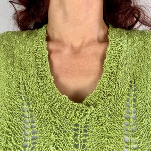 May include: Close-up of a lime green knit sweater with a deep V-neck. The sweater has a textured, open-weave design with a chevron pattern. The neckline and shoulders are visible.