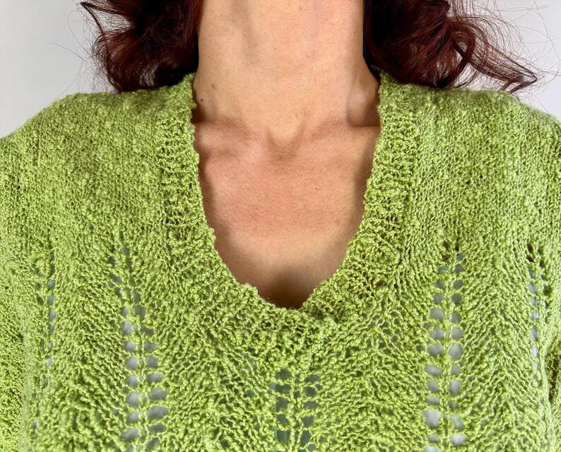 May include: Close-up of a lime green knit sweater with a deep V-neck. The sweater has a textured, open-weave design with a chevron pattern. The neckline and shoulders are visible.