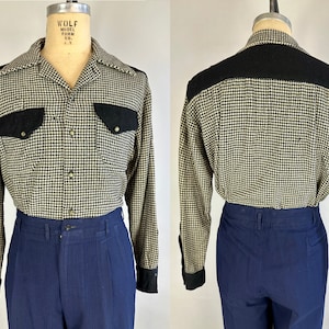 May include: A long-sleeved button-down shirt with a black and white houndstooth pattern. The shirt has black suede accents on the collar, yoke, and pockets. The shirt is on a mannequin wearing blue pants. "WOLF MODEL FORM CO. N.Y." is printed on the mannequin's neck.