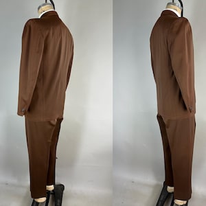 May include: A brown suit, consisting of a blazer and matching trousers, displayed on a mannequin. The blazer has a two-button closure and long sleeves. The trousers are straight-legged. The suit is a solid, medium brown color.