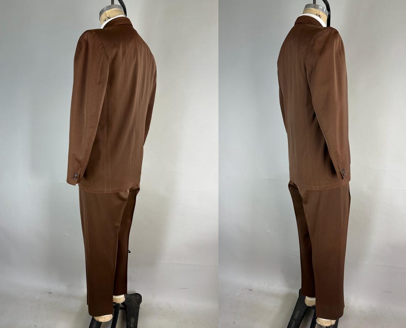 May include: A brown suit, consisting of a blazer and matching trousers, displayed on a mannequin. The blazer has a two-button closure and long sleeves. The trousers are straight-legged. The suit is a solid, medium brown color.