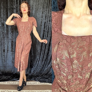 May include: A vintage knee-length dress in a dusty rose color with a floral pattern. The dress features short sleeves and a square neckline. The fabric has a subtle sheen, and the dress is fitted at the waist.