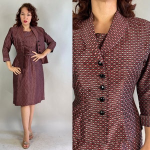 May include: A vintage two-piece dress suit in a geometric pattern of burgundy, white, and black. The suit includes a knee-length dress and a matching jacket with three-quarter sleeves and black buttons. The dress has a fitted bodice and a slight peplum.