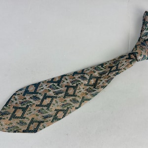 May include: A necktie featuring a repeating geometric pattern of dark blue squares on a tan background, accented with small patches of green and silver textured fabric. The tie is pre-knotted and displays a woven finish throughout the entire surface.