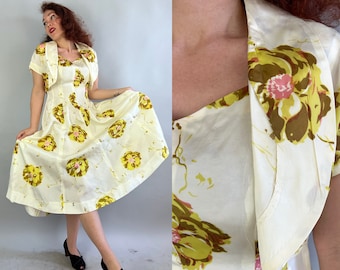 May include: A white dress with a floral print in shades of yellow and green. The dress has a fitted bodice and a full skirt. It also includes a matching jacket with short sleeves.