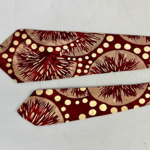 May include: Two neckties with a repeating pattern of red and beige fan-like shapes and white polka dots. The ties are on a white background. The ties are likely made of silk or a similar material.