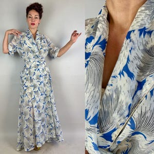 May include: A vintage, floor-length dress with a wrap-style bodice and short sleeves. The dress features a white background with a blue and gray floral pattern. The fabric appears lightweight and flowing, with a subtle sheen.