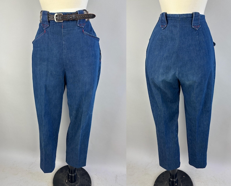 May include: High-waisted blue denim trousers featuring a dark brown leather belt with a silver-toned buckle. The pants have a structured waistband with belt loops, deep side pockets with red stitching accents, and a tapered leg silhouette.