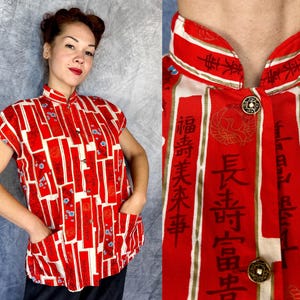 Pode incluir: Uma camisa sem mangas com bot&otilde;es, apresentando um padr&atilde;o vibrante em vermelho e creme com blocos retangulares verticais, caracteres de caligrafia chinesa em preto e pequenos detalhes florais azuis. Inclui gola mandarim e dois bolsos frontais.