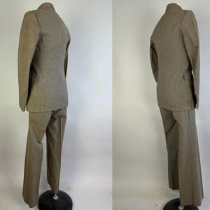 Op de afbeelding: Een tweedelig pak in een effen lichtbruine kleur, bestaande uit een blazer met lange mouwen en een ingekeepte revers, en een bijpassende broek van volledige lengte. Het pak wordt getoond op een etalagepop, met de rug- en zijaanzichten.