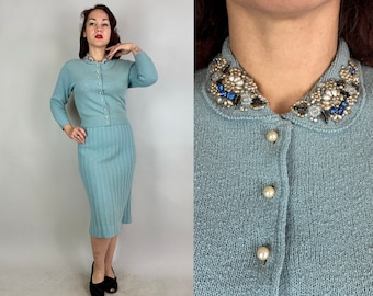 May include: A light blue knit two-piece set, featuring a long-sleeved cardigan with pearl buttons and a matching pencil skirt. The cardigan collar is embellished with beads and rhinestones. The outfit is a vintage style.