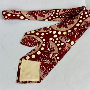 May include: A maroon tie featuring a repeating pattern of beige half-circles and white polka dots. The tie is made of a silky material. The tie's design is a vintage style.