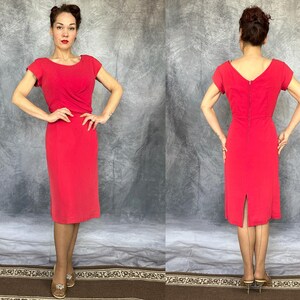 May include: A solid red knee-length dress featuring short sleeves, a boat neckline, and a fitted bodice with subtle draping at the waist. The back of the dress displays a central vertical zipper closure and a small slit at the hemline.
