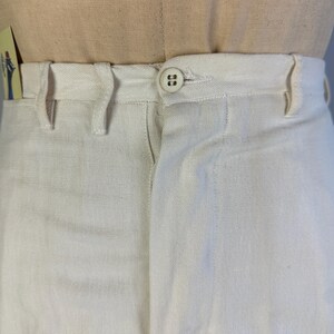 May include: Off-white trousers featuring a high-waisted design with a single button closure at the centre front. The trousers include belt loops along the waistband and a visible fly construction, presented on a neutral-toned mannequin torso.